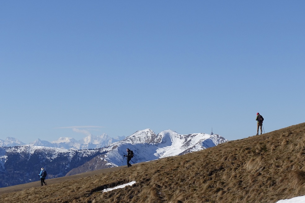 Escursionisti iniziano la discesa, sullo sfondo il Monte Tamaro