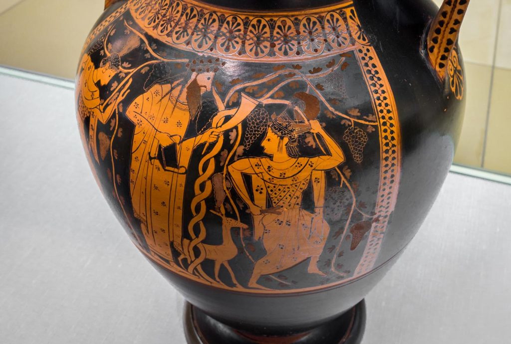 Anfora tramandata dagli Etruschi con Dionisio tra due menadi danzanti tra i rami contorti di una vigna; esposta al Museo di Monaco.(ArchaiOptix)