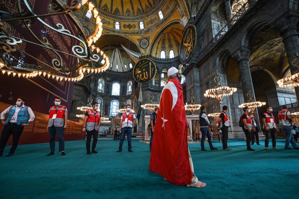 Un uomo avvolto nella bandiera turca visita, in occasione dalla prima preghiera musulmana, la basilica di Santa Sofia a Istanbul tornata alla funzione di moschea (AFP)