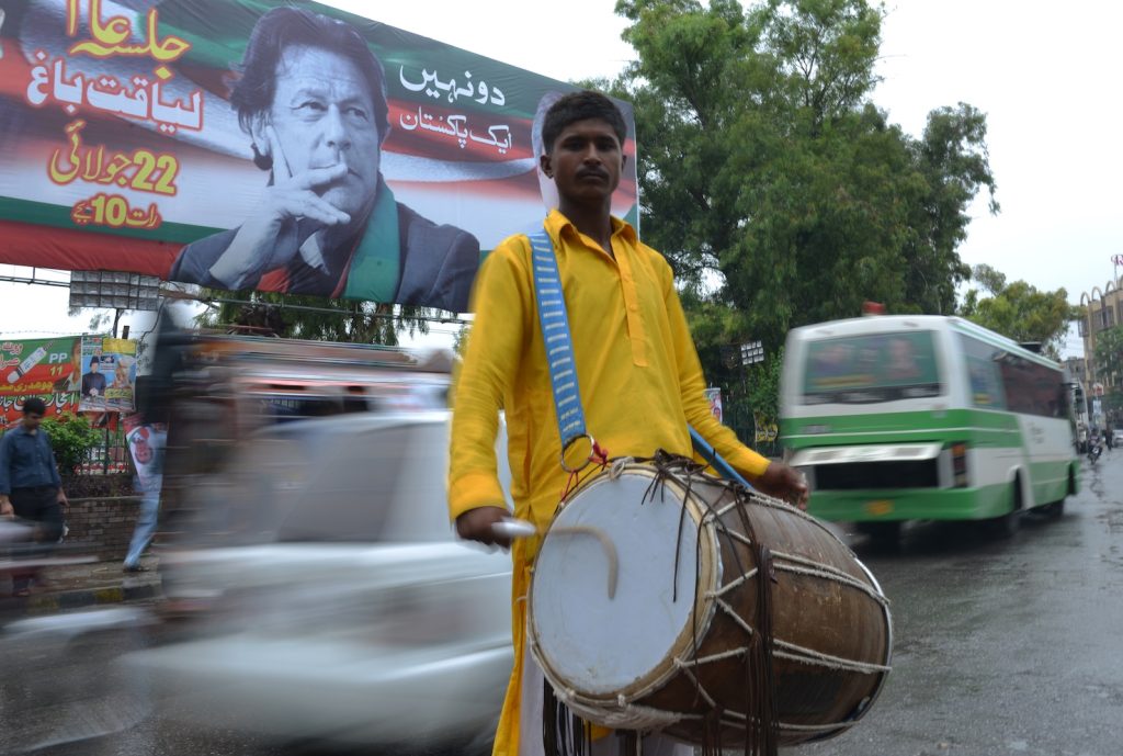 Suonatore di tamburi si esibisce a Rawalpindi davanti a un manifesto elettorale con il volto di Imran Khan (AFP)