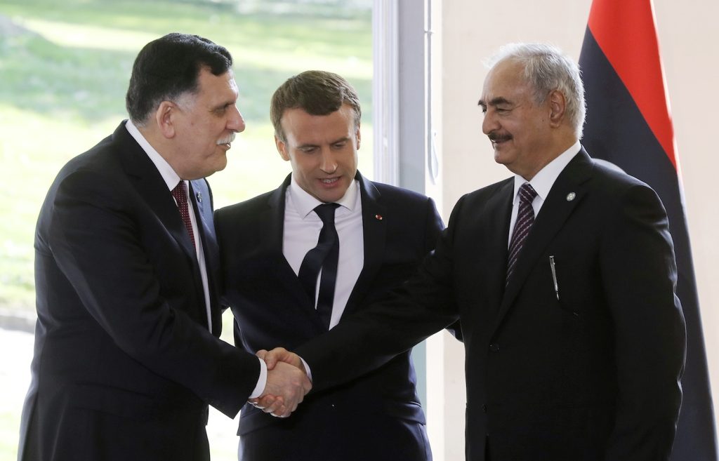 Emmanuel Macron (centro) osserva la stretta di mano fra il premier libico Fayez al-Sarraj (sinistra) e il generale Khalifa Haftar (AFP)