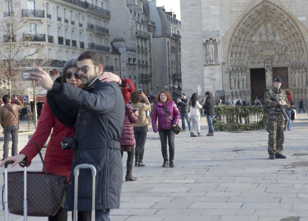 Una coppia di turisti si fa un selfie davanti alla cattedrale di Notre Dame a Parigi, presidiata dai soldati francesi (Keystone)