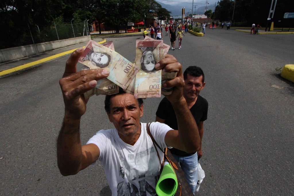 Un uomo mostra alcune banconote da 100 bolivares, che rappresentano il 48% del denaro contante in Venezuela (AFP)