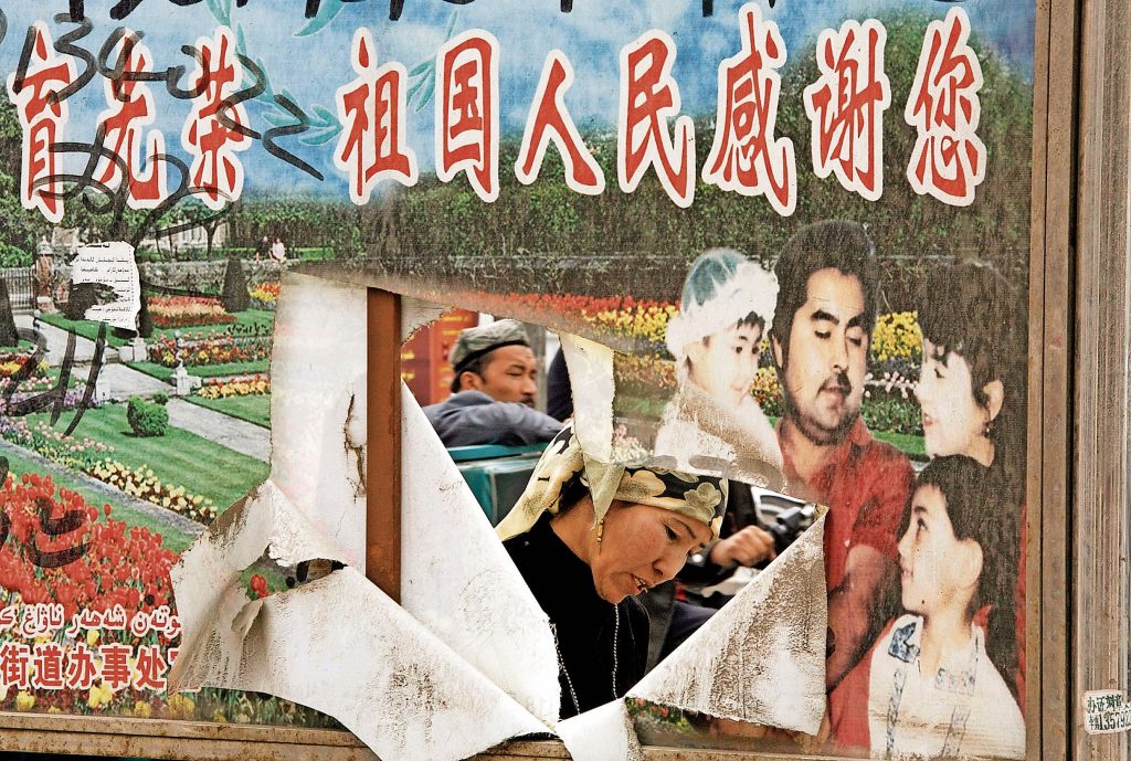 Una donna e un uomo uiguri nello Xinjiang. Davanti a loro, un cartellone della propaganda cinese che recita: «La madrepatria e il popolo ti apprezzano» (Keystone)