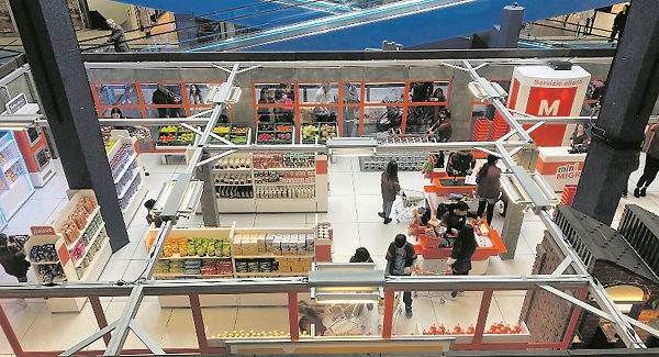 Bambine in fila in cassa al mini supermercato Migros del Serfontana; a destra, il mini supermercato visto dall’alto. (Ame Valsa)