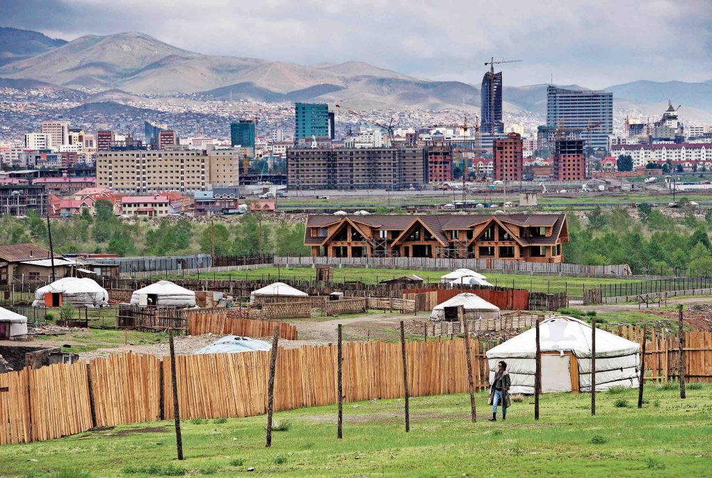 1. Una donna cammina davanti a una yurta e, sullo sfondo, la capitale della Mongolia Ulan Bator